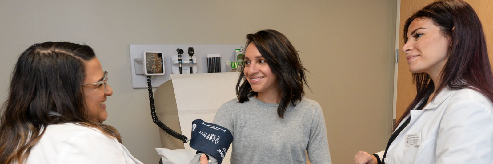 two female nursing students practicing as you try to finding a female patients blood pressure